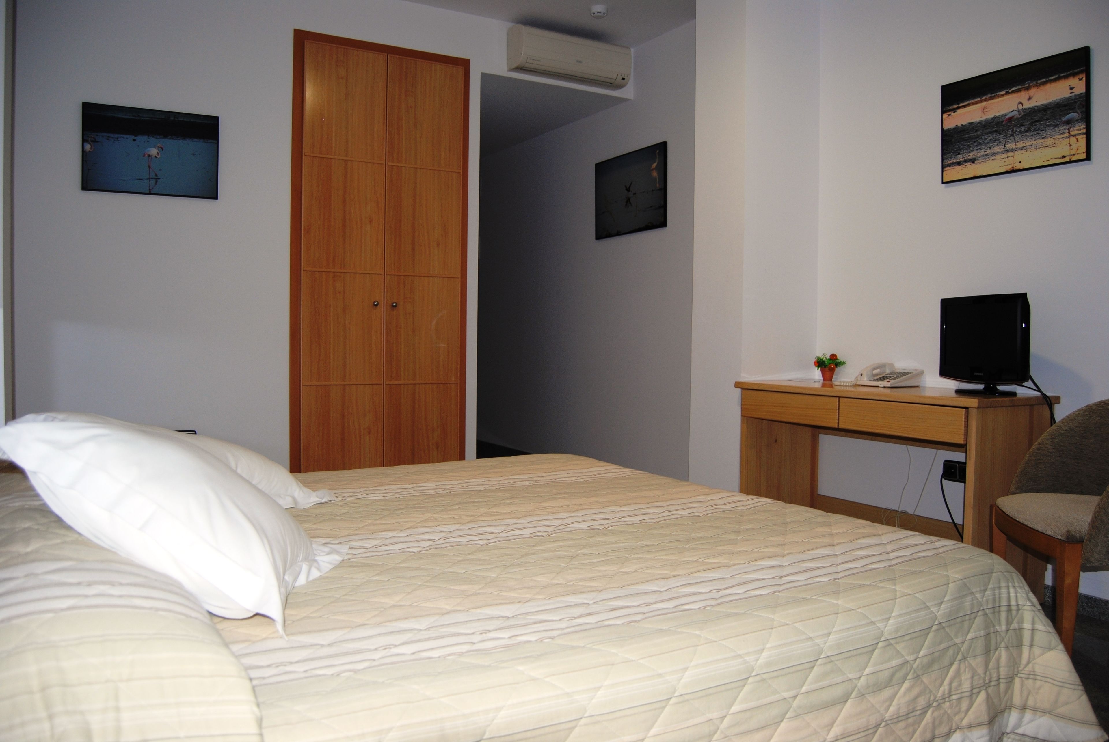 A bedroom with a bed, a wooden wardrobe, a desk with a computer, and a chair.