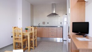 A compact kitchen with wooden cabinets, a stainless steel range hood, a built-in oven, and a dining area with a wooden table and chairs. - Hotel Albanta (La Lantejuela)