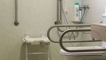 Une salle de bain équipée de toilettes accessibles aux personnes en fauteuil roulant, de barres d’appui et d’une douche avec un pommeau de douche amovible.
