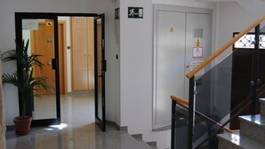 A clean, modern lobby with a glass staircase, a potted plant, and a wooden door leading to another room. - Hotel Albanta (La Lantejuela)