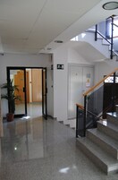 Un vestíbulo limpio y moderno con una escalera de cristal, una planta en maceta y una puerta de madera que da a otra habitación.