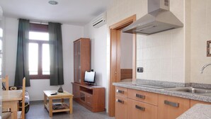 A compact kitchen with wooden cabinets, a granite countertop, and a built-in oven. - Hotel Albanta (La Lantejuela)