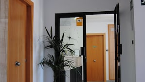 A hallway with a potted plant, wooden doors, and a mirror reflecting a room with a desk and chair. - Hotel Albanta (La Lantejuela)