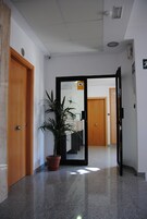 Un pasillo con una planta en maceta, puertas de madera y un espejo que refleja una habitación con un escritorio y una silla.