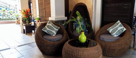 A seating area with wicker chairs and a central table, surrounded by potted plants and decorative pillows.