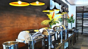 A buffet setup with multiple food dispensers, a vase with flowers, and a wooden wall in the background.