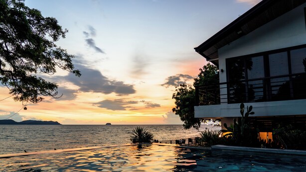 A modern building with a pool overlooking a body of water at sunset.