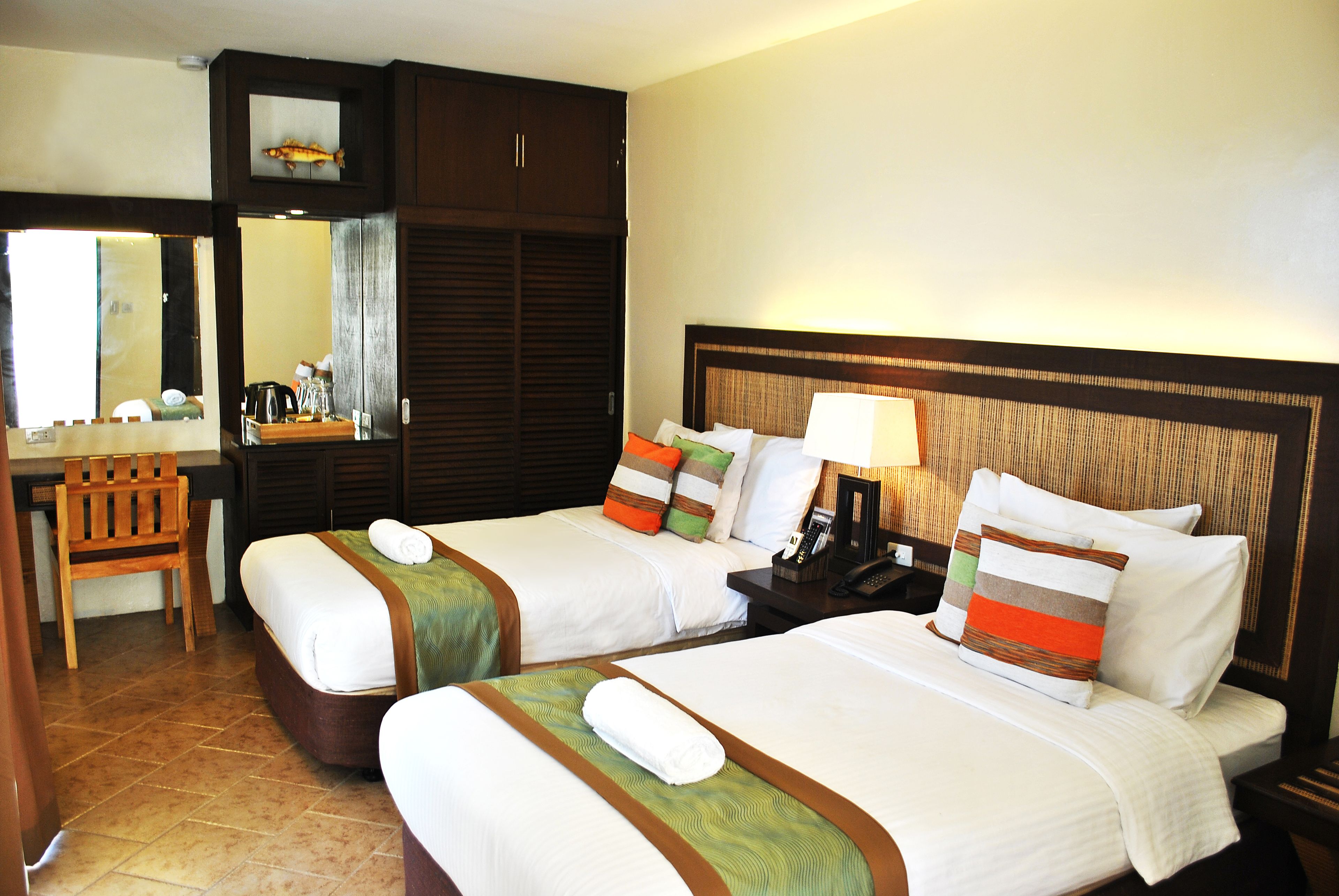 A hotel room with two beds, a desk, and a mirror.