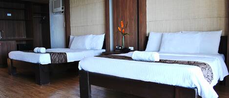 Two single beds with wooden frames and white bedding, a small table with a vase of flowers, and a wardrobe in a hotel room.
