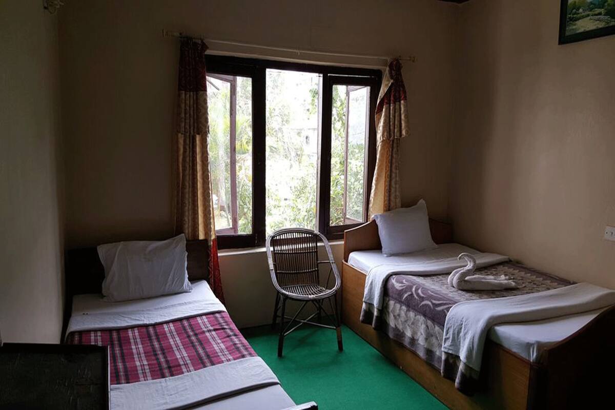 Une chambre avec deux lits simples, une chaise et une fenêtre avec des rideaux.