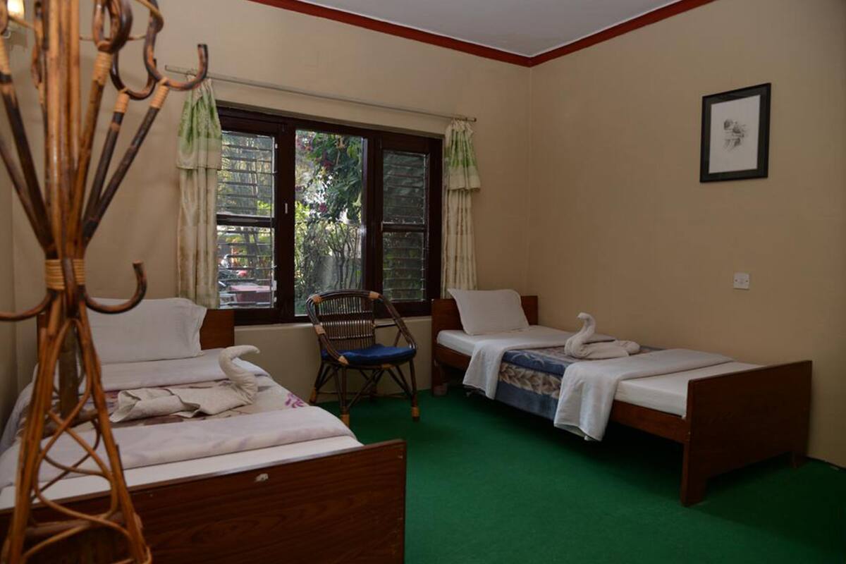 Une chambre avec deux lits simples, une chaise, une fenêtre avec des rideaux et un tableau encadré au mur.
