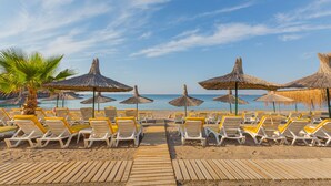 A beachside area with rows of sun loungers and thatched umbrellas, a wooden walkway, and a clear view of the sea.
