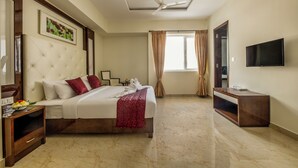 Habitación de hotel con cama, televisor, ventilador de techo y ventana con cortinas.