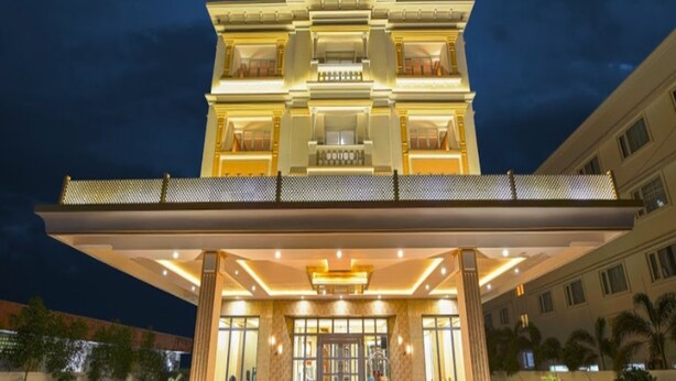 Un hotel de varios pisos con una entrada imponente, un corredor cubierto y un jardín bien cuidado.