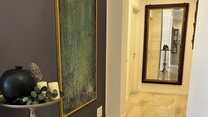 A hallway with a large abstract painting, a decorative table with candles, and a mirror reflecting a room. - Fleur Blanche (Verona)