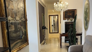 A spacious living room with a beige sofa, a chandelier, and a large painting of a fountain. - Fleur Blanche (Verona)