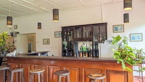 A bar area with wooden counter, stools, hanging lights, and framed pictures on the wall. - Kitulgala Heritage Rest House (Kithulgala)