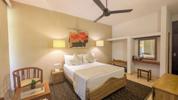 A hotel room with a bed, bedside table, chair, desk, and a ceiling fan. - Kitulgala Heritage Rest House (Kithulgala)