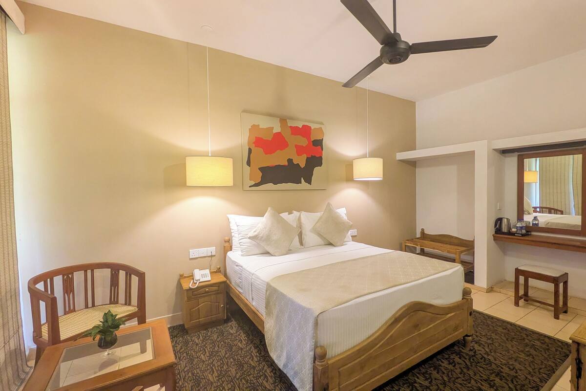 A hotel room with a bed, bedside table, chair, desk, and a ceiling fan.