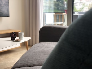A modern living room with a grey sofa, a small round table with a white mug and a decorative item, and a view of a balcony with a railing. - Grey Pearls Suites (Jounieh)