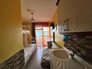 Une chambre d’hôtel compacte comprenant un lit superposé, une kitchenette, un évier et une fenêtre avec des rideaux.