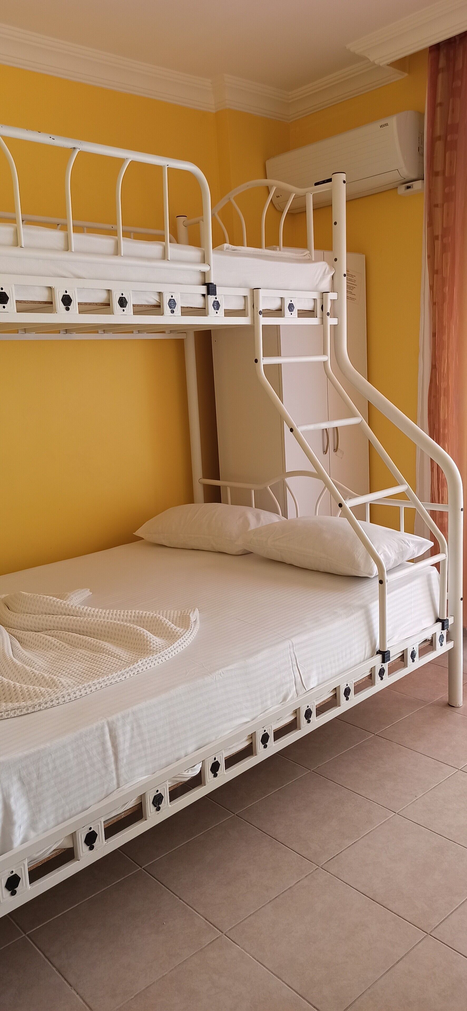 Una cama litera con escalera, un colchón blanco y una manta blanca.