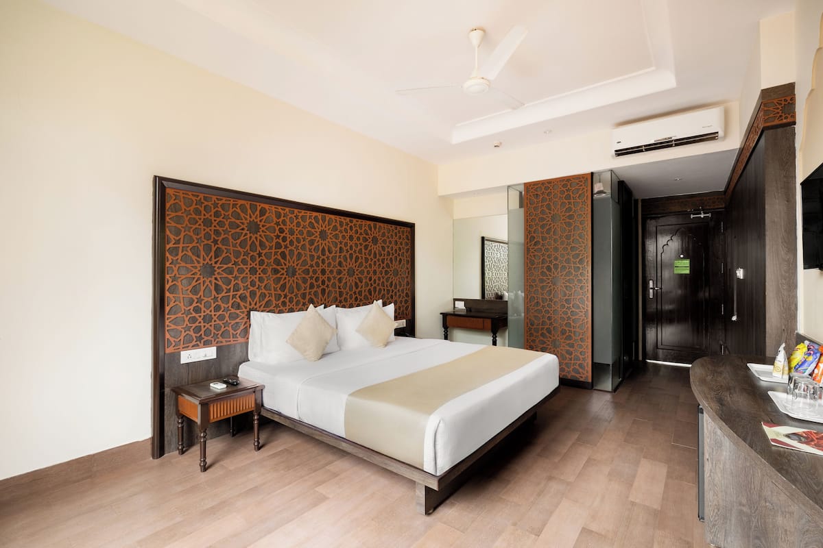 A hotel room with a large bed, a nightstand, a desk, and a mirror.