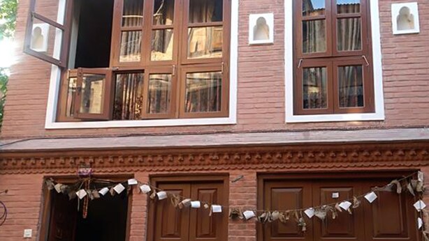 A two-story building with a brick facade, large wooden doors, and multiple windows. - Malla Guest House (Bhaktapur)