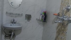 A bathroom with a sink, mirror, shower, and toiletries. - Malla Guest House (Bhaktapur)