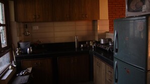A compact kitchen with wooden cabinets, a refrigerator, and a microwave. - Malla Guest House (Bhaktapur)