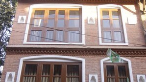 A multi-story building with a brick facade, large windows with white frames, and a balcony with a metal railing. - Malla Guest House (Bhaktapur)