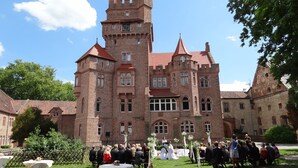 Un castillo histórico con una torre central, rodeado de un césped cuidado y una multitud de personas.