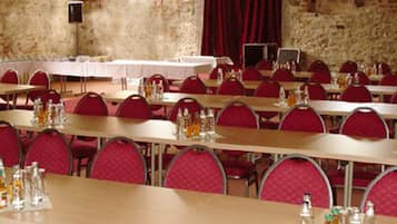 A conference room with multiple tables and red chairs, set against a stone wall backdrop.