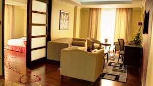 A hotel room with a bed, two armchairs, a small table, and a desk with a lamp.