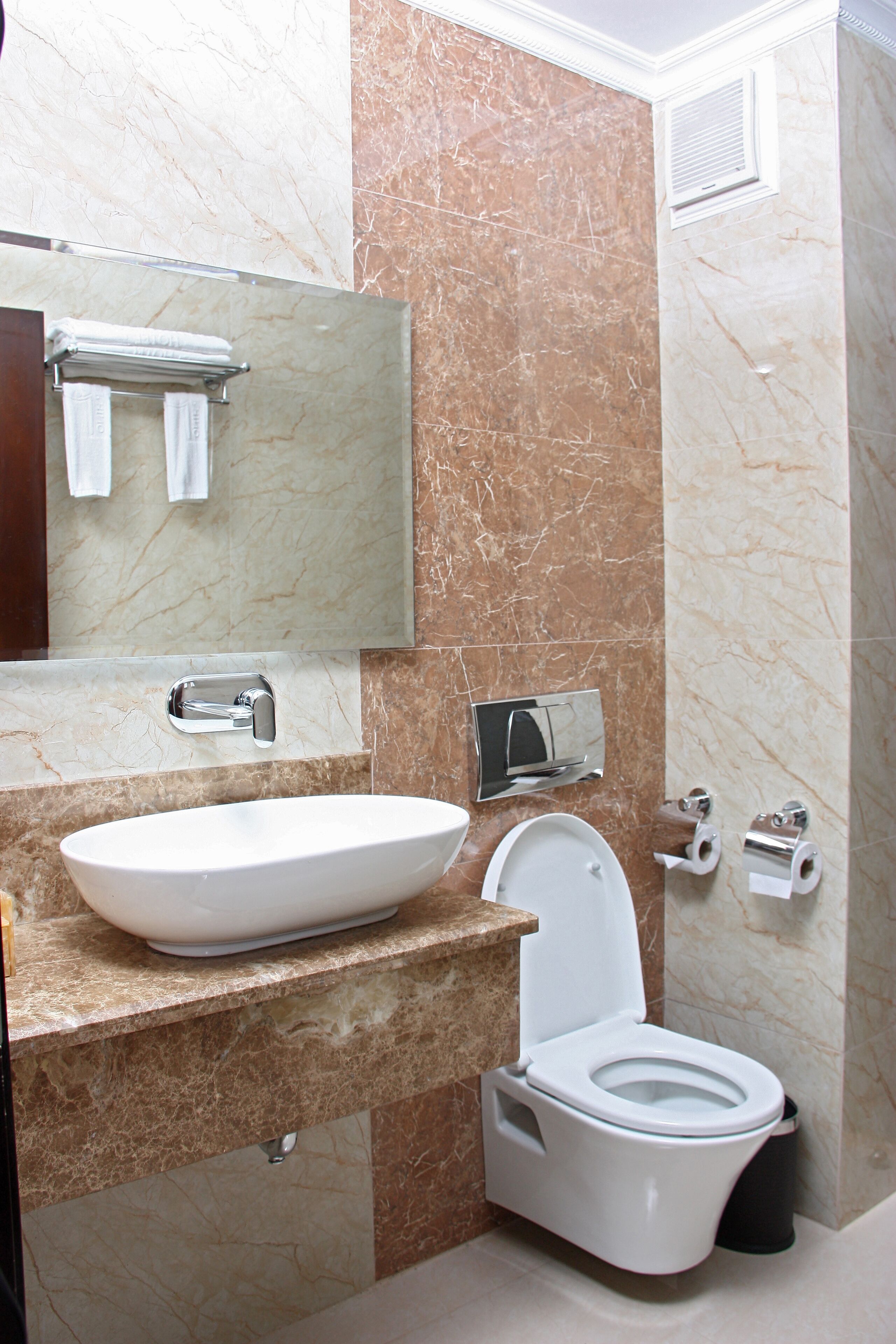 A bathroom with a marble sink, a toilet, and a mirror.