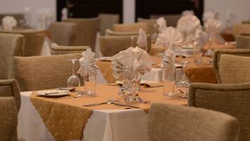 A banquet hall with round tables set with white tablecloths, glassware, and folded napkins.
