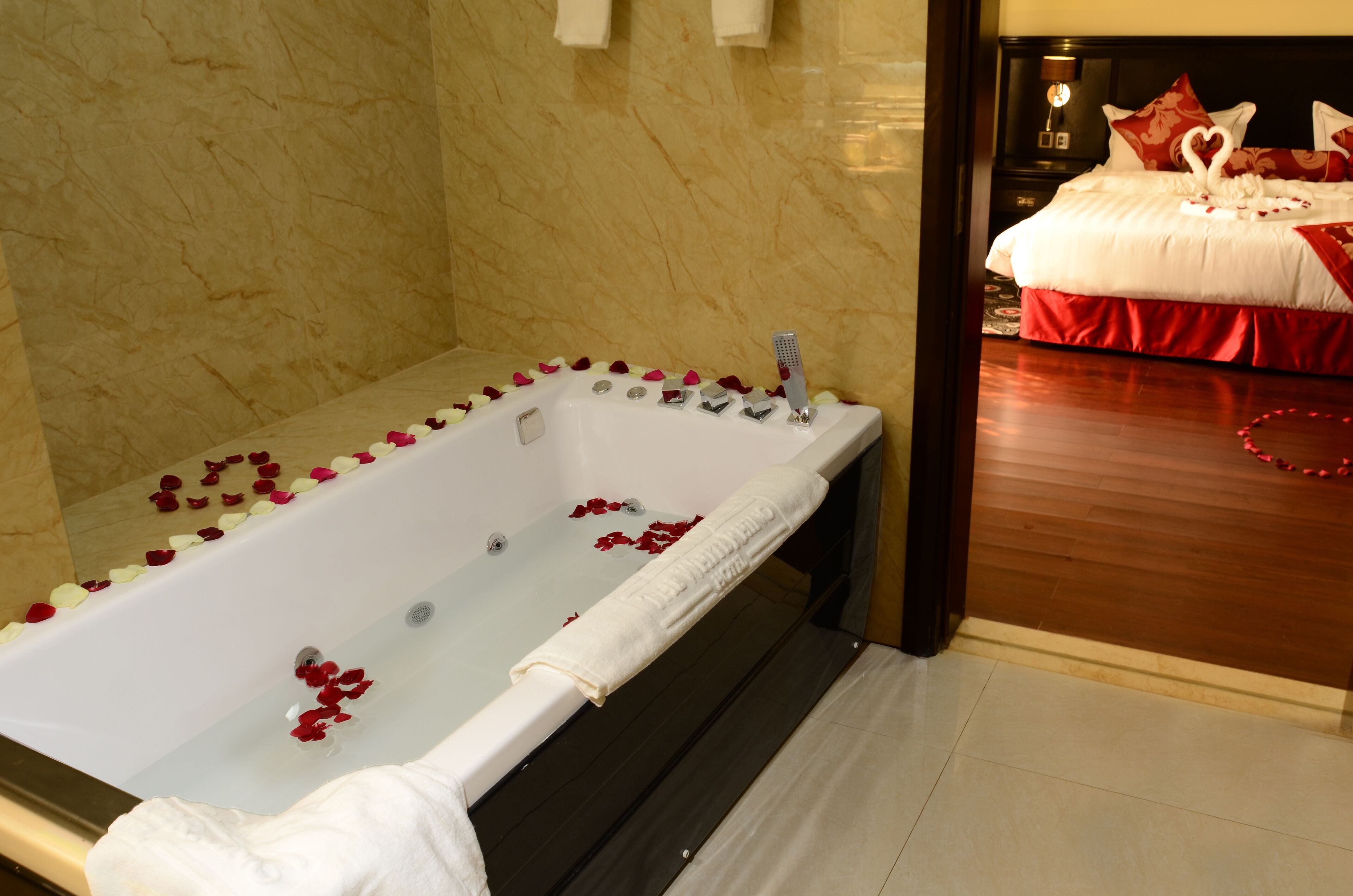 Habitación de hotel con baño de mármol, piso de madera y cama con ropa de cama roja.