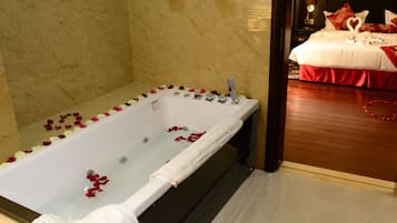 Habitación de hotel con baño de mármol, piso de madera y cama con ropa de cama roja.