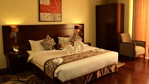 A hotel room with a large bed, two bedside lamps, a headboard, a chair, a painting on the wall, and a carpeted floor.