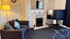 A living room with a fireplace, a sofa, a TV, and a lamp. - The Wellesley Apartment (Methil)