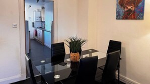A dining area with a glass table and black chairs, a potted plant, and a painting on the wall. - The Wellesley Apartment (Methil)