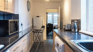 A compact kitchen with a microwave, toaster, and washing machine. - The Wellesley Apartment (Methil)