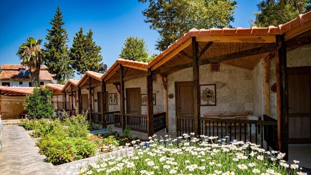 A row of traditional wooden cabins with tiled roofs, surrounded by a garden with white flowers. - Likya Adrasan (Kumluca)