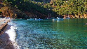 A coastal scene with boats anchored near the shore, a rocky hill in the background, and a clear sky. - Likya Adrasan (Kumluca)