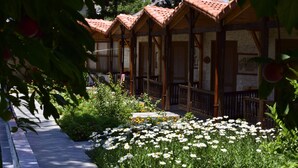 A row of wooden cabins with tiled roofs, surrounded by a garden with white and yellow flowers. - Likya Adrasan (Kumluca)