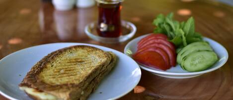 A plate of grilled toast, sliced tomatoes, and cucumbers on a wooden table.