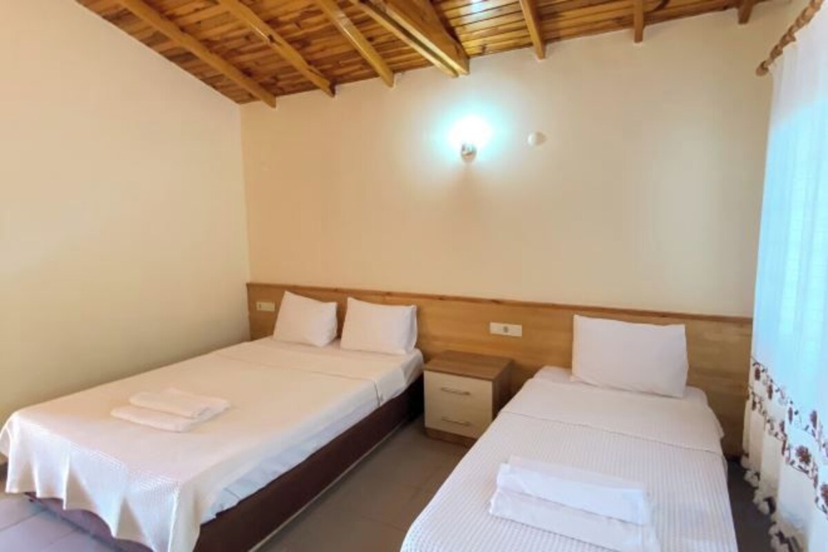 A room with two single beds, wooden headboards, a nightstand, and a wall-mounted light fixture.