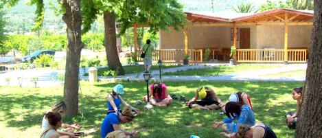 A group of people sitting on grass in a park-like setting with trees and a building in the background.