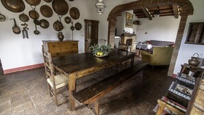Een rustieke eetkamer met een houten tafel, banken en divers hangend keukengerei.