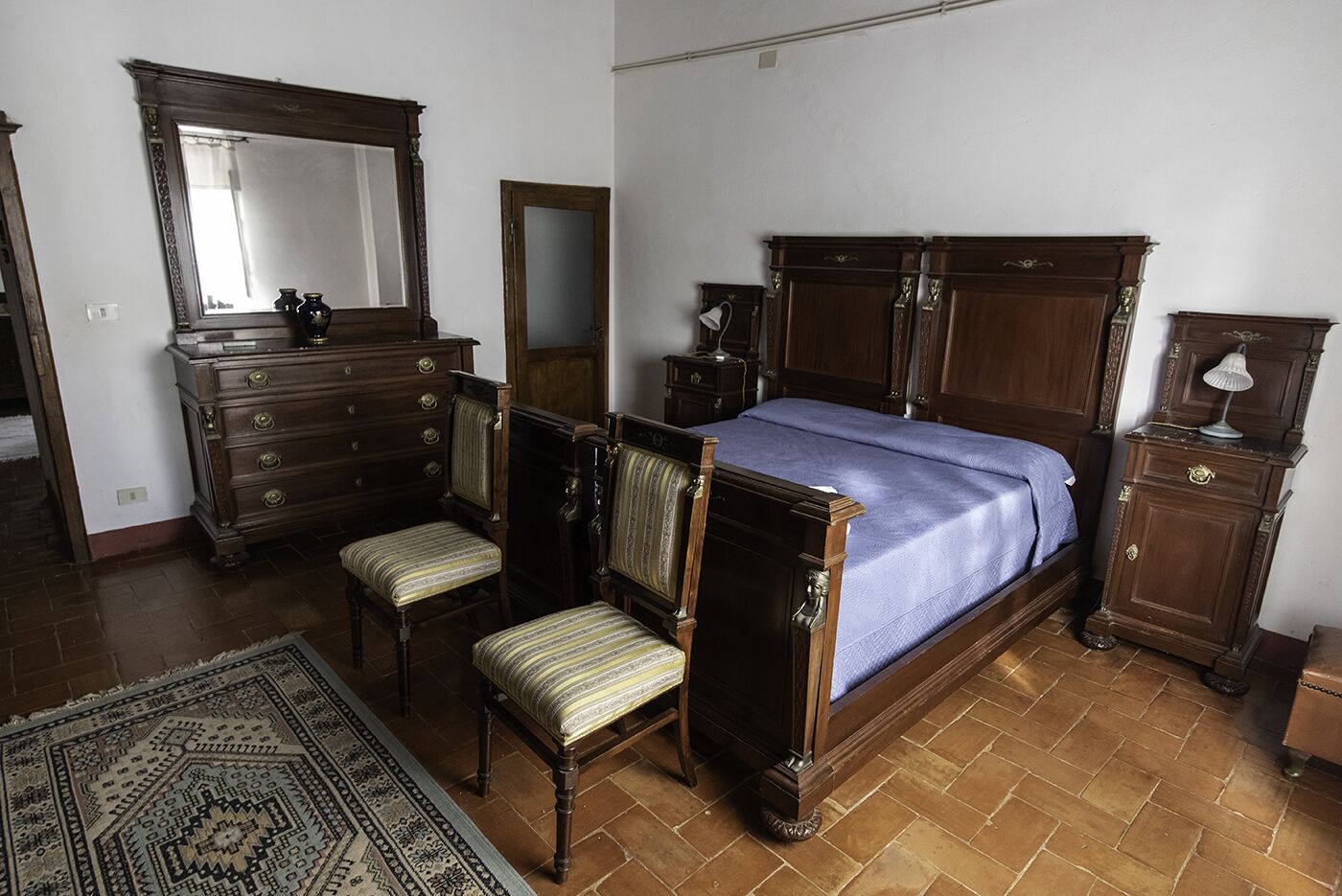 Une chambre à coucher avec un grand lit, deux chaises, une commode, un miroir et une lampe.